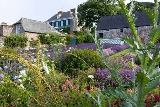 Vista panorámica de los jardines de Mothecombe House con flores coloridas y edificios históricos al fondo