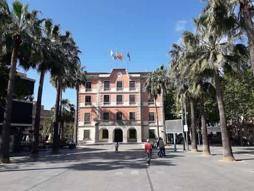 Vista frontal del Ajuntament de Castelldefels con palmeras y banderas