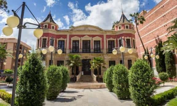 Fachada principal del Palacete Huerto Ruano durante el día con jardines y farolas decorativas