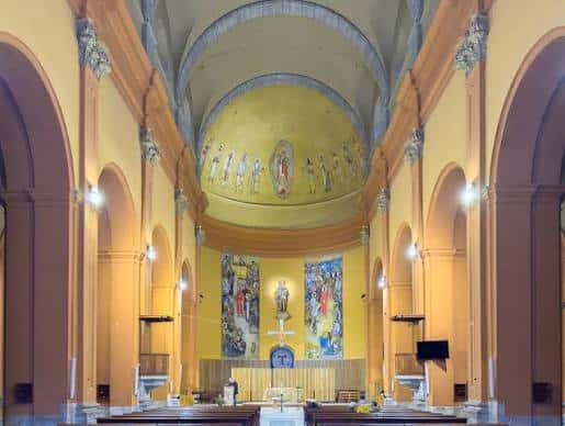 Interior de la iglesia con bóveda decorada, altar central y pinturas murales bajo iluminación cálida