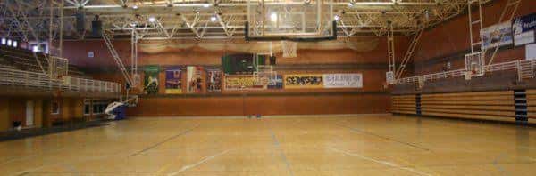 Pista deportiva interior vacía con canastas y gradas para eventos deportivos
