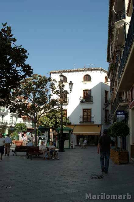 Plaza de Las Carmelitas con personas sentadas en bancos bajo árboles y arquitectura andaluza