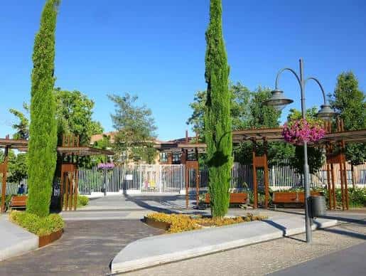 Entrada a la Plaza de Colón con pérgolas y cipreses altos bajo cielo despejado