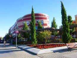 Plaza de Colón con edificio curvo rojo al fondo y bancas rodeadas de vegetación