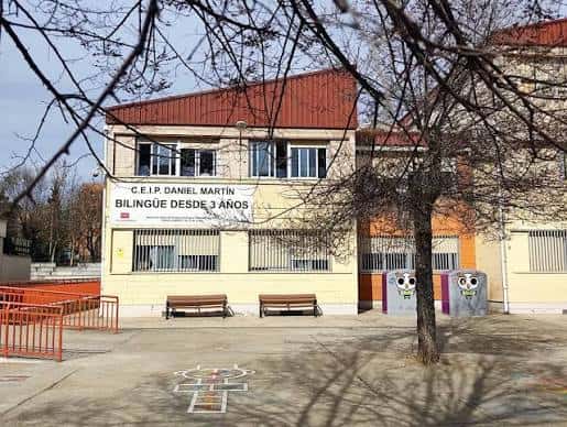 Fachada frontal del colegio con letrero 'Bilingüe desde 3 años' y patio con bancos y árboles sin hojas