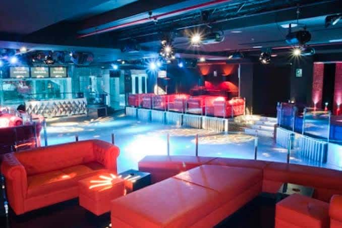 Interior del club con zona de sofás rojos y pista de baile iluminada