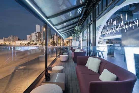 Terraza exterior del club con sofás morados y vistas al puerto nocturno