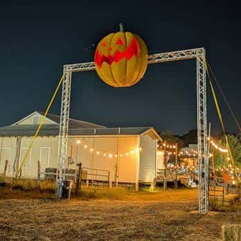 Entrada nocturna del evento con decoración de calabaza iluminada y luces festivas