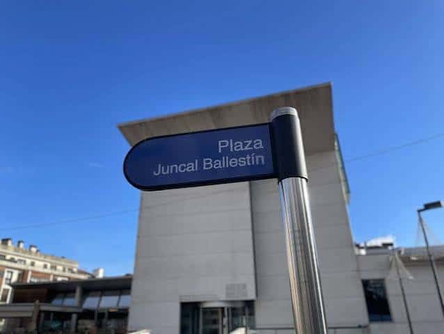 Señal de la Plaza Juncal Ballestín con el edificio moderno al fondo