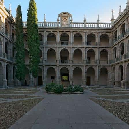 Vista panorámica del Patio de Santo Tomás de Villanueva con arcos y cipreses bajo cielo despejado