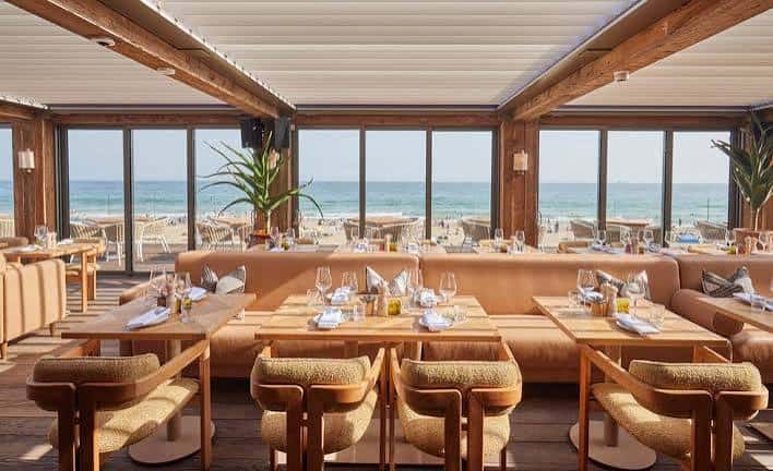Interior del restaurante con mesas dispuestas para cena y vistas al mar