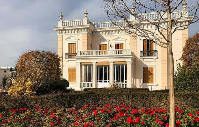 Plano medio del cartel de inauguración de los jardines con público asistente y bancos circulares