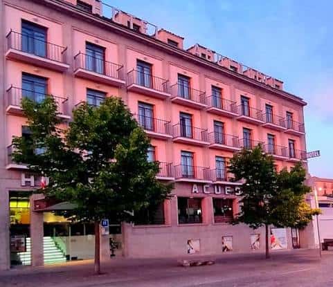 Fachada diurna del hotel en tonos rosados con árboles frente a la entrada