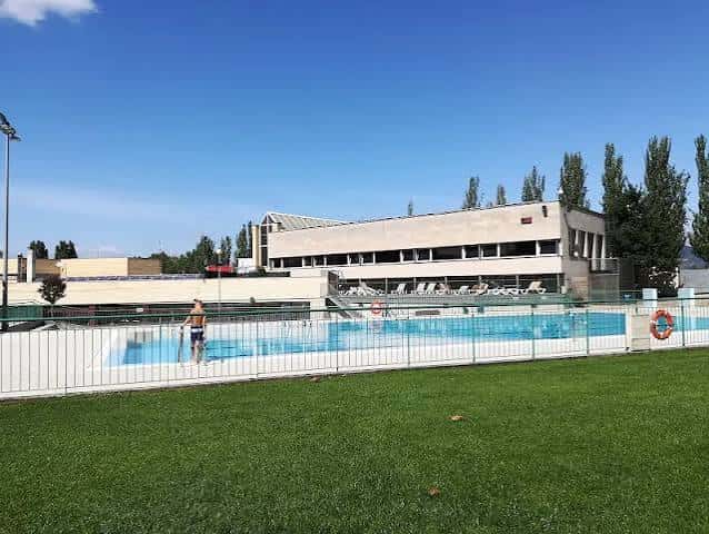 Vista general del complejo deportivo desde el exterior, mostrando la piscina y el edificio principal bajo cielo despejado