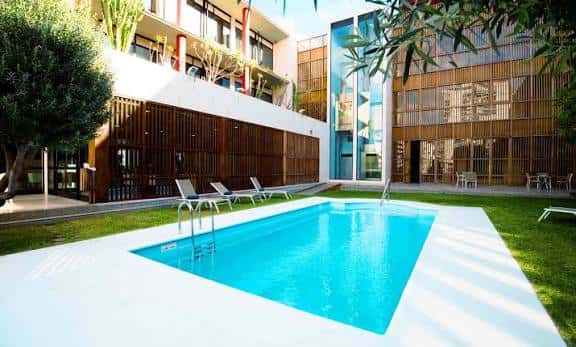 Vista diurna de la piscina exterior del hotel con tumbonas y jardines