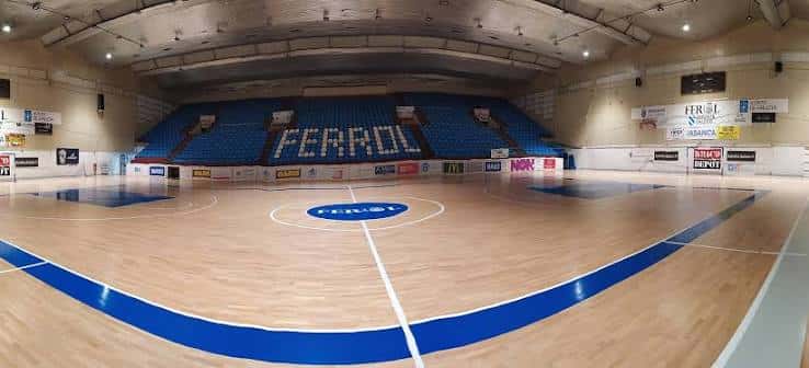 Interior del pabellón mostrando la cancha de baloncesto vacía y las gradas azules con el nombre 'FERROL'