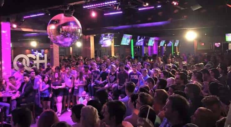 Interior del club lleno de gente con una bola de discoteca iluminando la pista
