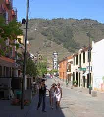 Vista panorámica de la calle que conduce a la Plaza de San Bartolomé, con edificios coloridos y montañas al fondo