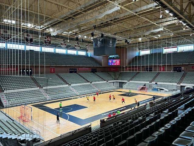 Interior del pabellón vacío mostrando la cancha de baloncesto y gradas modernas