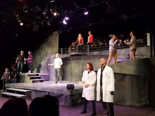 Escenario del teatro durante una representación teatral con actores en múltiples niveles
