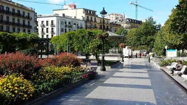 Camino peatonal en la Plaza Easo con jardines floridos y arquitectura urbana al fondo