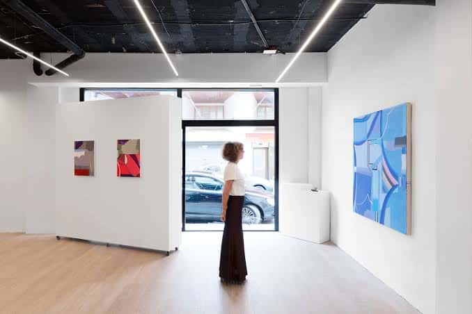 Interior de la galería con obras de arte abstracto y una visitante contemplando