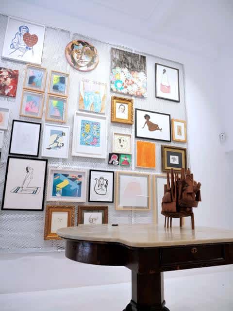 Pared de la galería con múltiples cuadros enmarcados y escultura sobre mesa