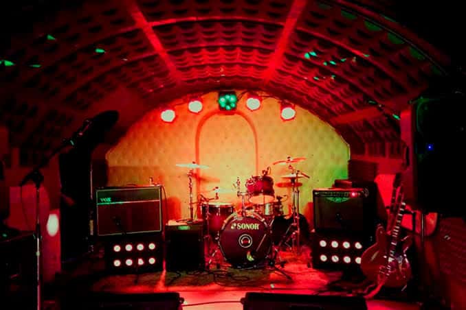 Escenario montado con batería y amplificadores bajo luces rojas