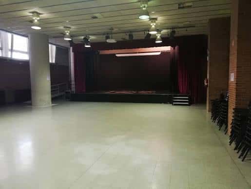 Sala de actos vacía con escenario, cortinas rojas e iluminación profesional