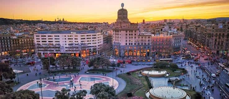 Vista panorámica de la Plaza de Catalunya al atardecer con edificios históricos iluminados
