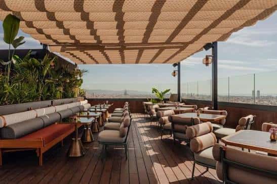 Terraza exterior del hotel con mobiliario moderno, pérgola textil y vistas al horizonte urbano