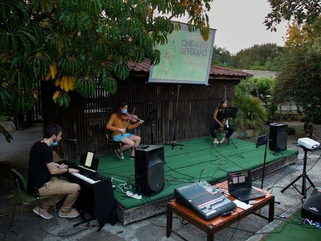 Concierto al aire libre con trío musical y pantalla de cine en entorno natural