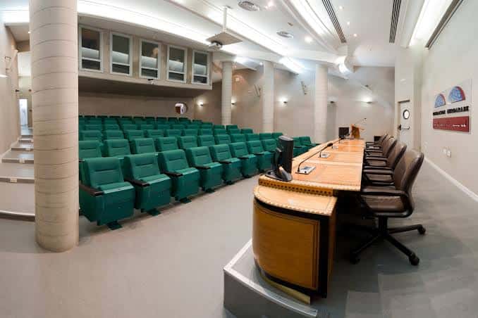 Sala de conferencias con butacas verdes y mesa directiva