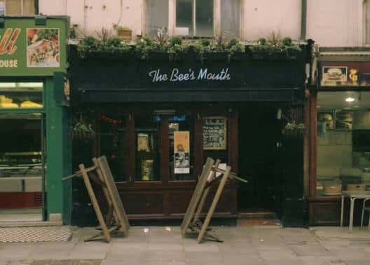 Fachada exterior de The Bee's Mouth con toldo negro y macetas