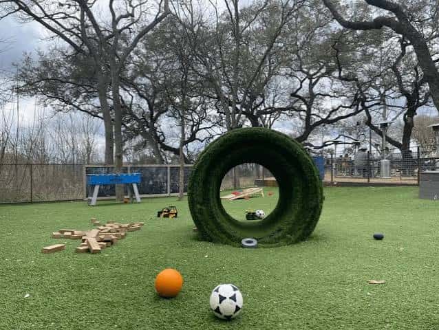 Área de juegos al aire libre con césped artificial, juguetes y estructuras para niños