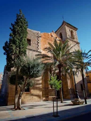 Fachada principal de la Iglesia de San Mateo en Lorca con palmeras y cielo azul