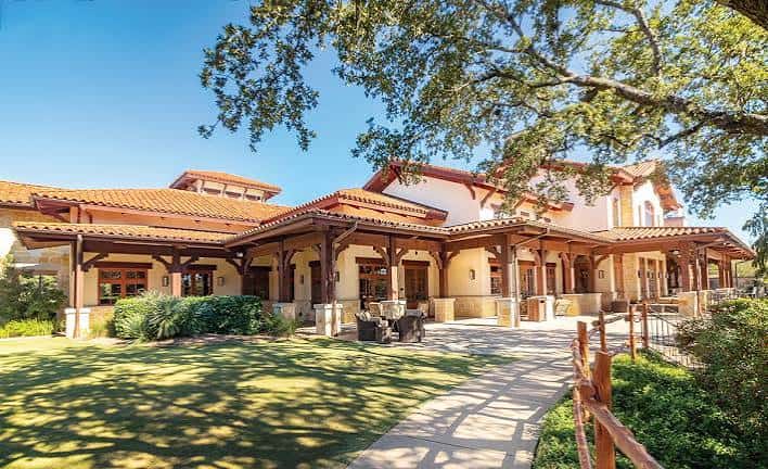 Fachada diurna del club house con porches de madera y jardines verdes