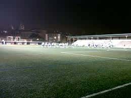 Vista nocturna del campo de fútbol municipal con gradas y césped iluminado