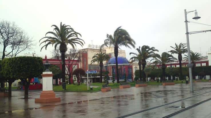 Plaza de la Alameda en un día lluvioso con edificios rojos al fondo