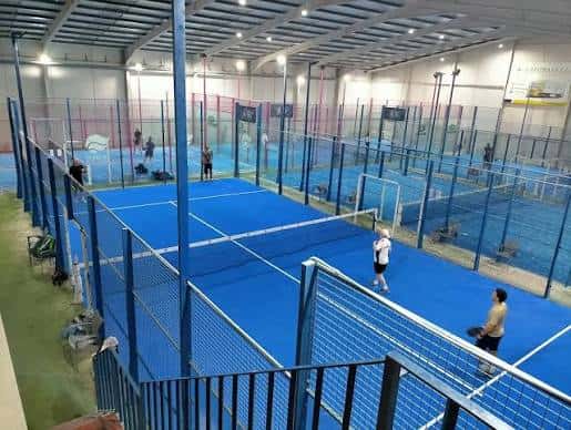 Vista interior de las pistas de pádel con suelo azul y jugadores en acción
