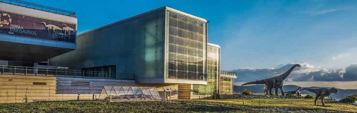 Vista panorámica exterior del Museo Paleontológico con esculturas de dinosaurios al atardecer