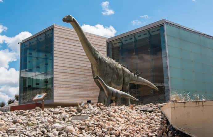 Fachada moderna del museo con estatua de saurópodo en primer plano bajo cielo azul