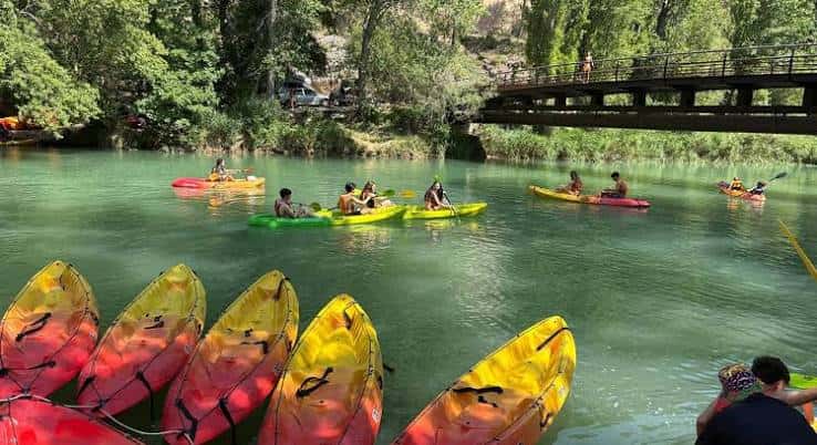 Grupo de personas practicando piragüismo en el río con una pasarela al fondo