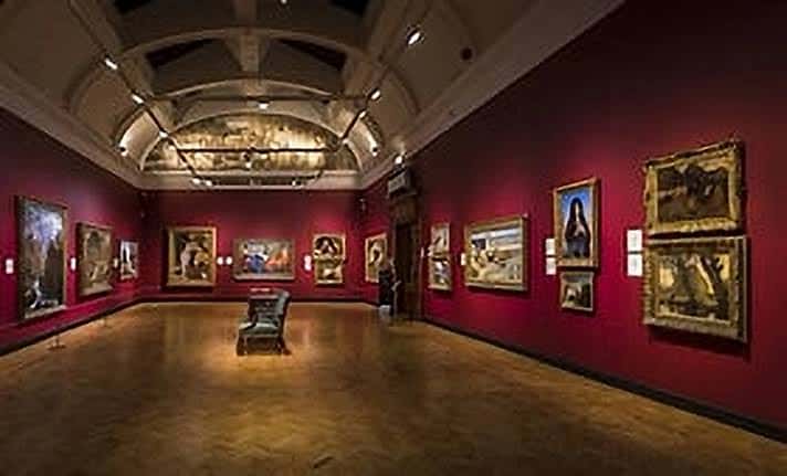 Sala principal de exposiciones con paredes rojas y obras clásicas enmarcadas
