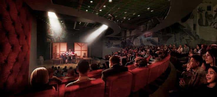 Interior del auditorio durante una función teatral con público sentado en butacas rojas y escenario iluminado