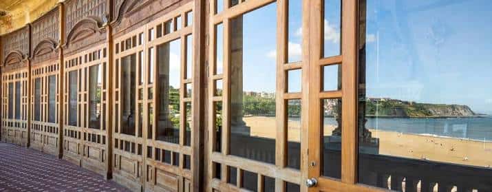 Vista del interior de las galerías con grandes ventanales de madera y vistas al mar
