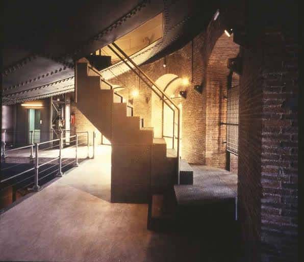 Interior industrial con escalera metálica y paredes de ladrillo, ideal para eventos temáticos