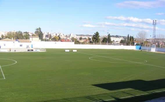 Vista panorámica del campo de fútbol con gradas y ciudad al fondo