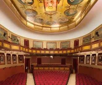 Vista panorámica del salón principal con techo pintado y butacas rojas