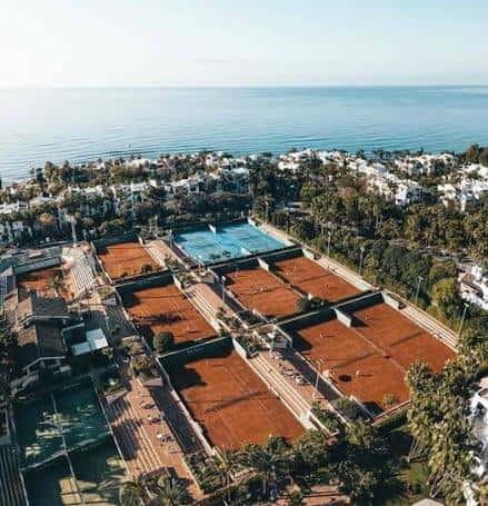 Vista aérea de las pistas de tenis y pádel del Puente Romano con el mar al fondo
